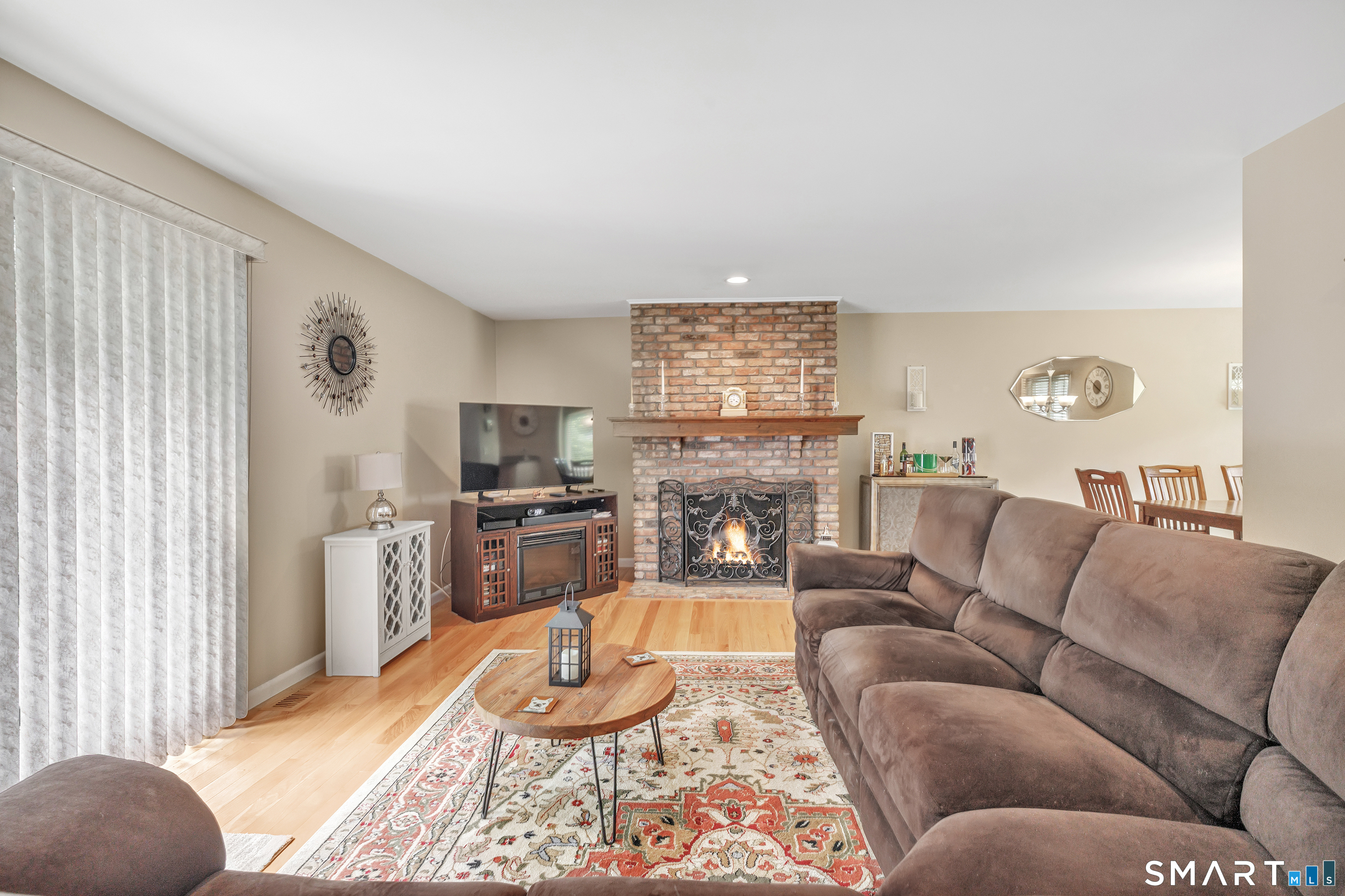 Furnished living room with a brick fireplace, lit fire, and large brown sectional sofa.