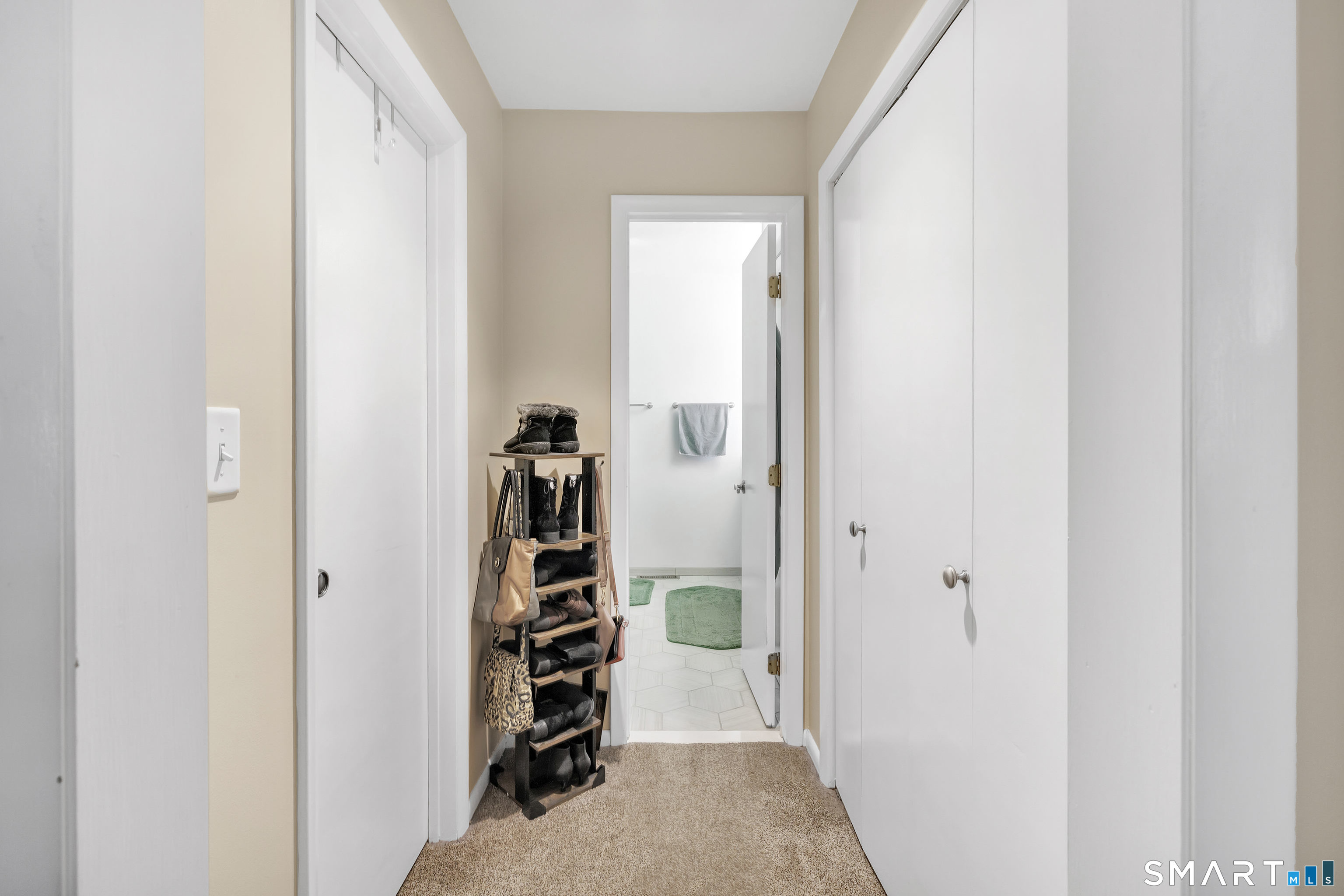 Carpeted hallway with white closets, a shoe rack, and an open bathroom doorway.