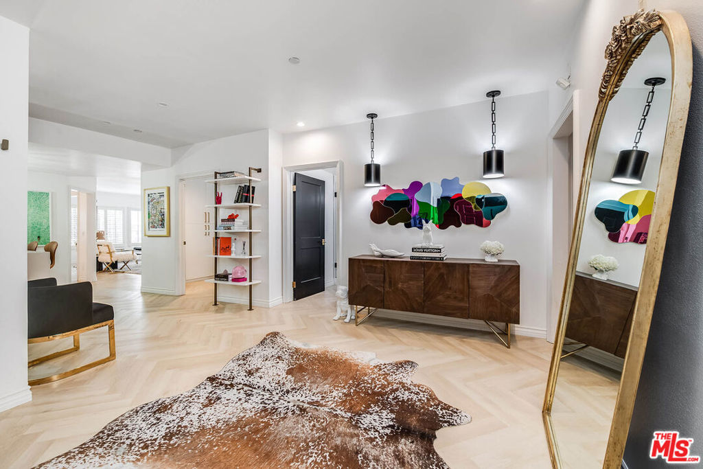 Bright condo entry with a wood console, colorful abstract art, and an ornate gold-framed mirror.