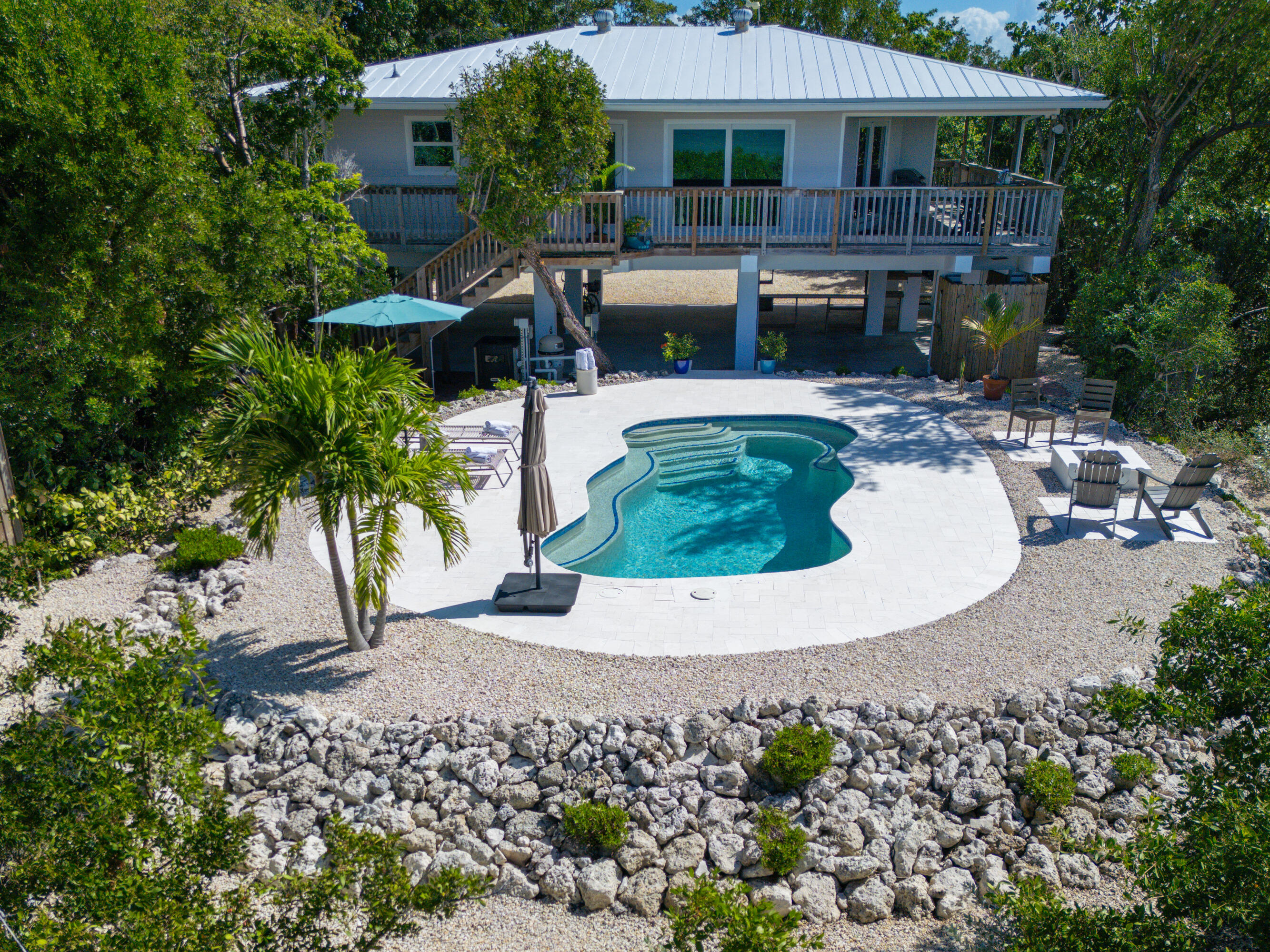 Raised home and wooden deck overlooking a freeform pool amid palms and dense greenery.