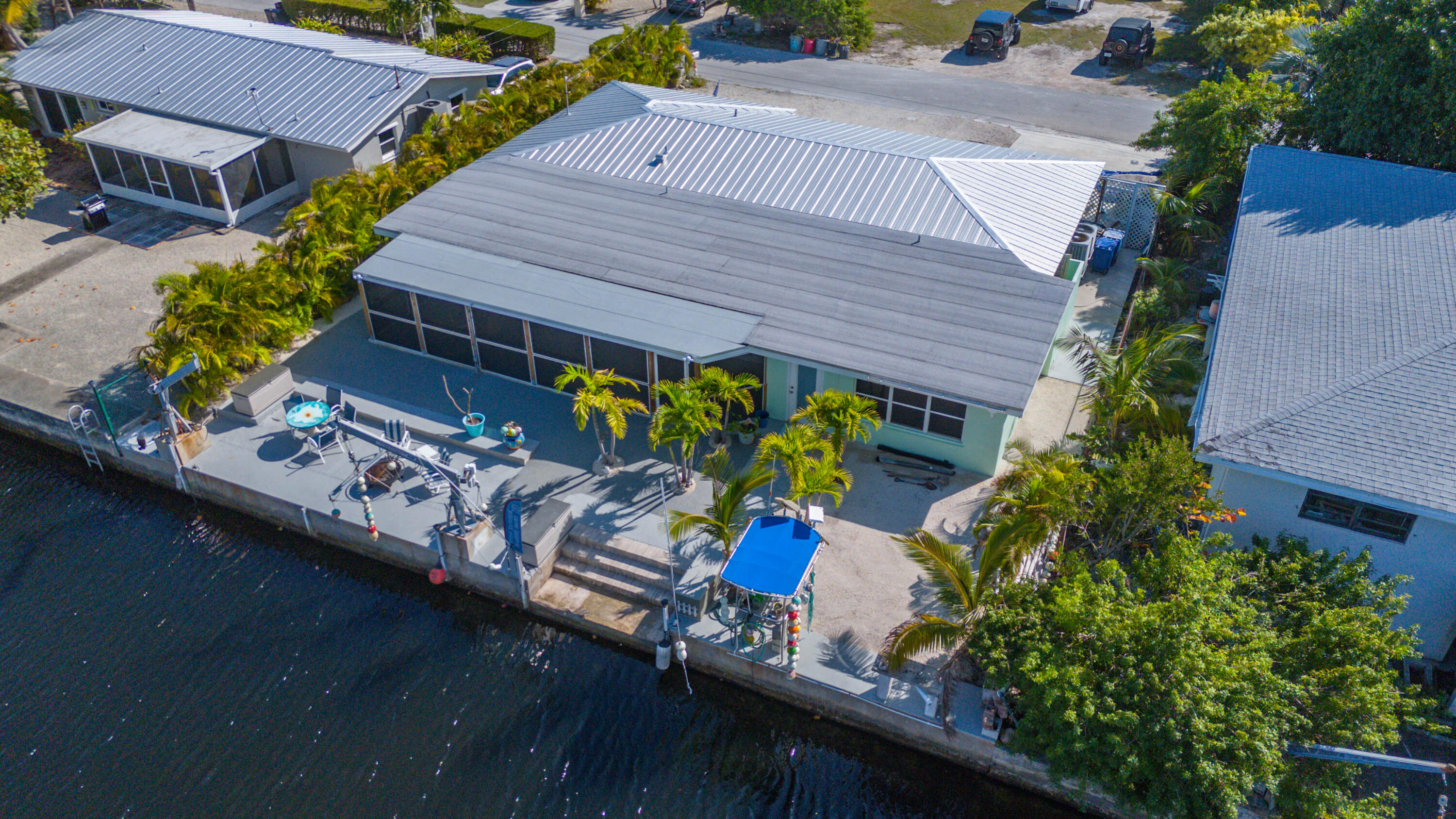 Aerial view of a canal-front home with a screened patio, palm trees, and outdoor seating.