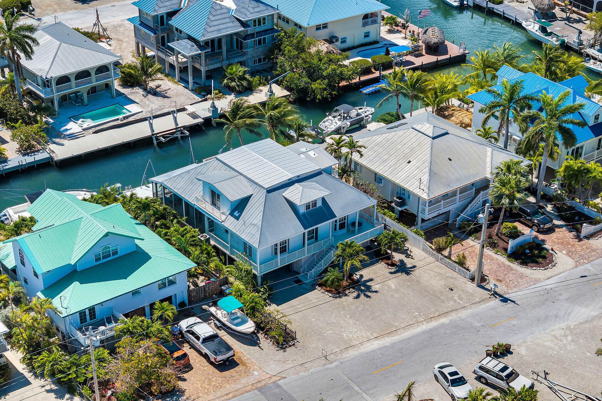 Aerial view of canal-side homes with blue roofs, palm trees, docks, and boats.