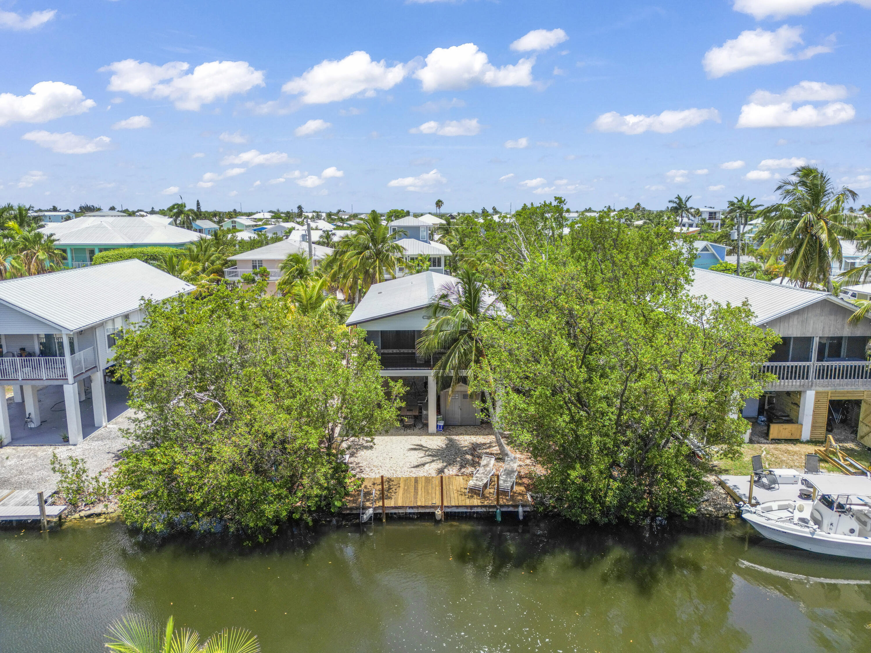 Canal-front home with a wooden dock, palm trees, and a boat on the canal.