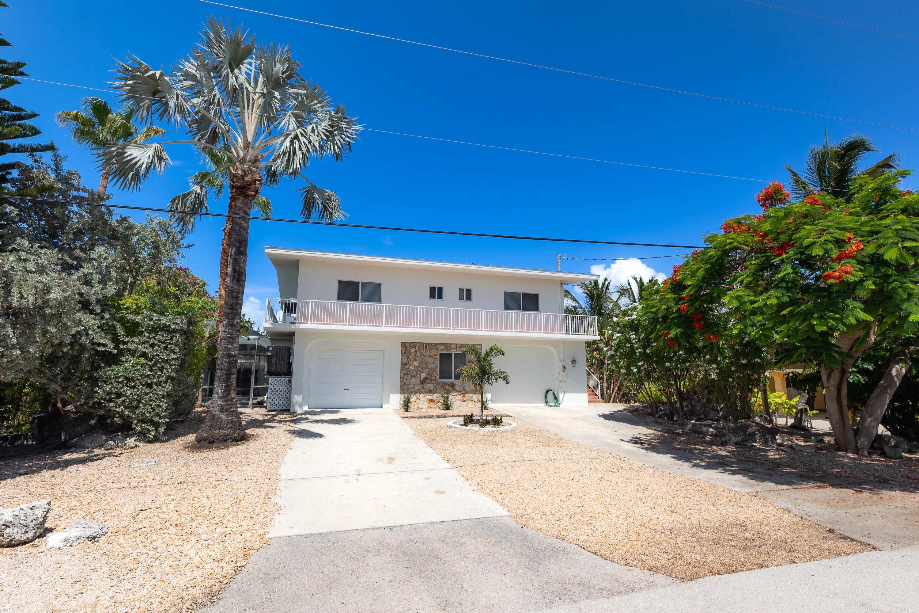 Two-story white home with a long balcony, stone facade accents, and tropical landscaping.