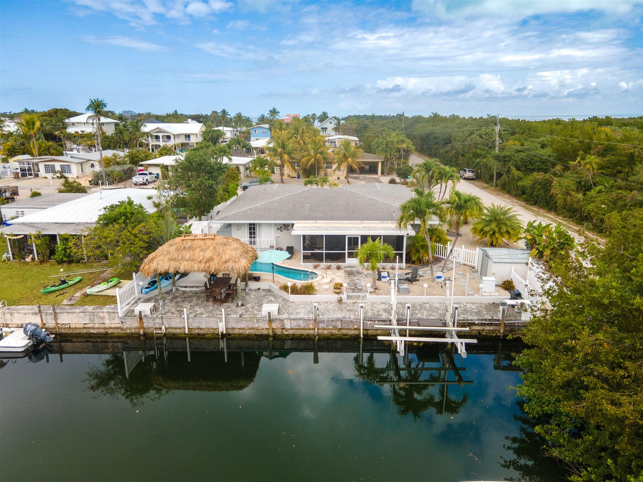 Aerial view of a canal-front home with a pool, tiki hut, and dock.