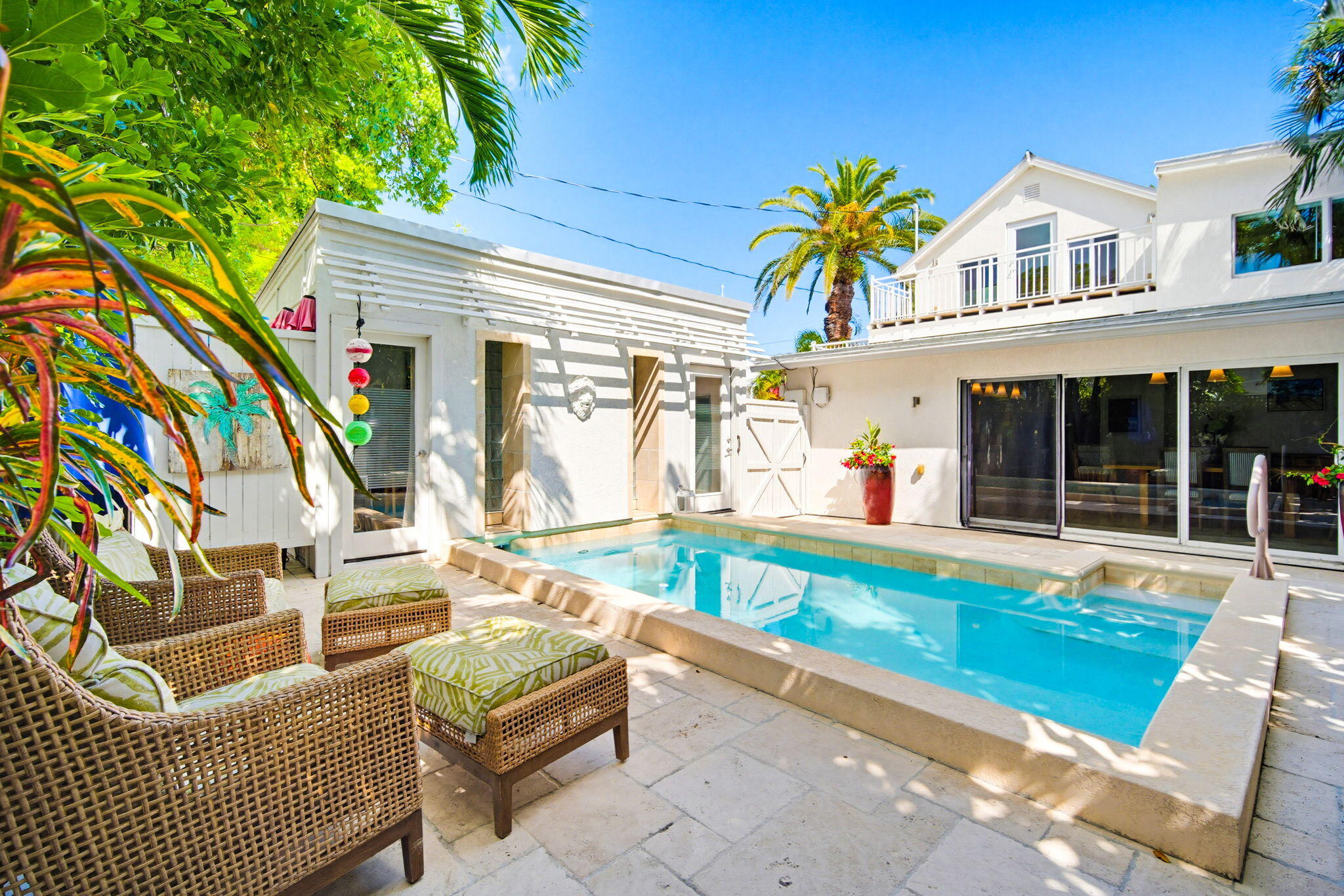 White two-story home around a pool, with wicker patio seating and tropical landscaping.