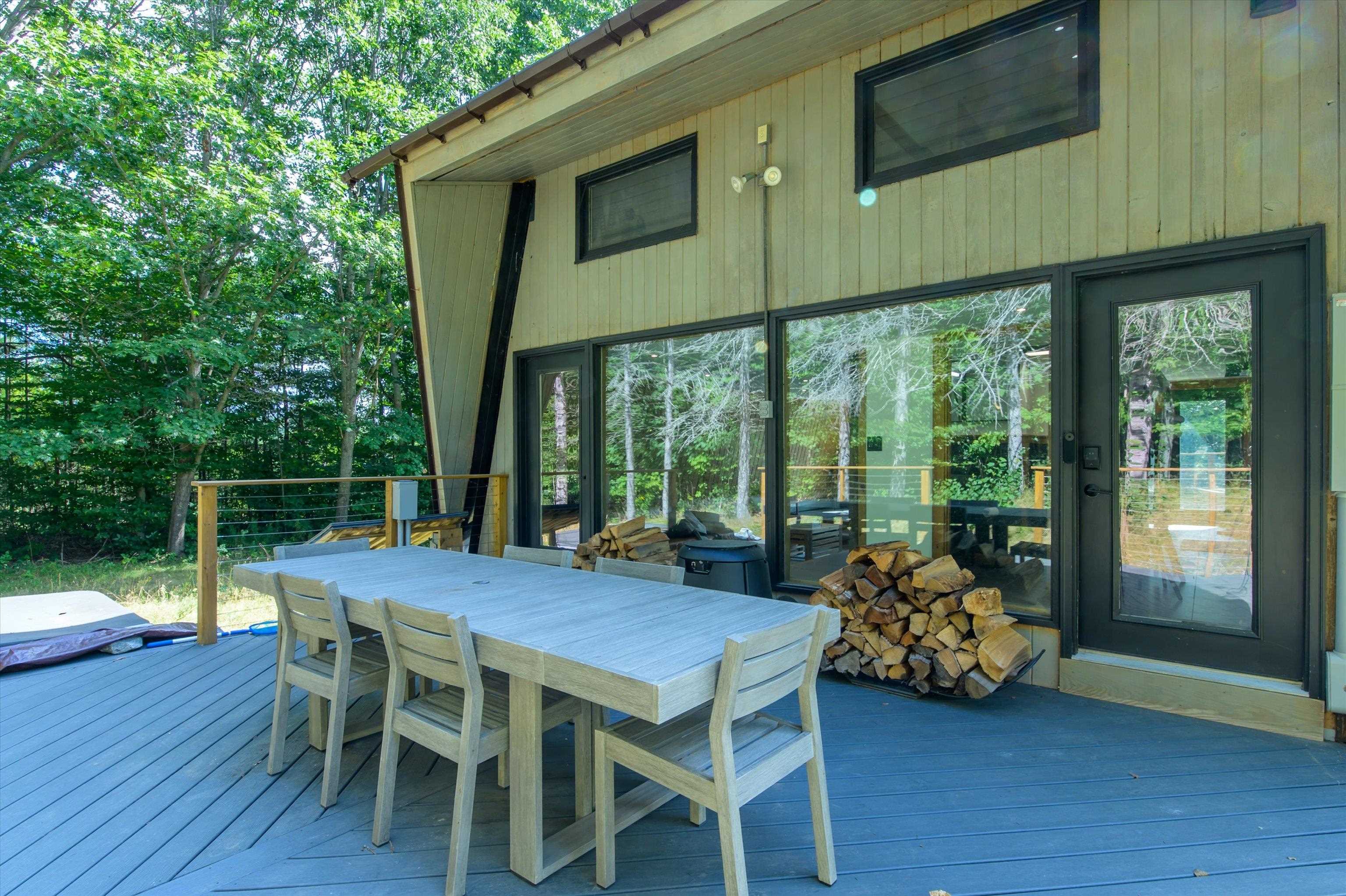 Modern home's wooded deck with a dining set, large glass doors, and stacked firewood.