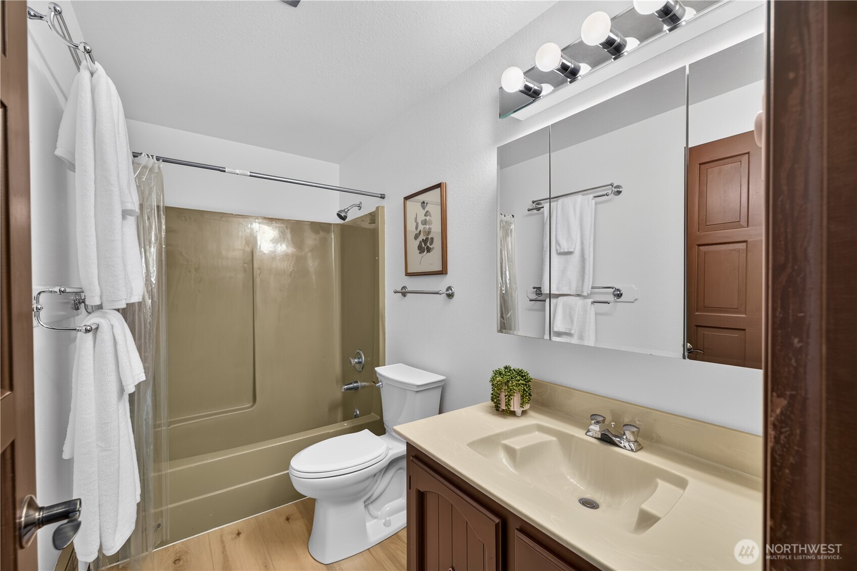 Bathroom with tan tub and shower, mirrored cabinet, and single-sink vanity.