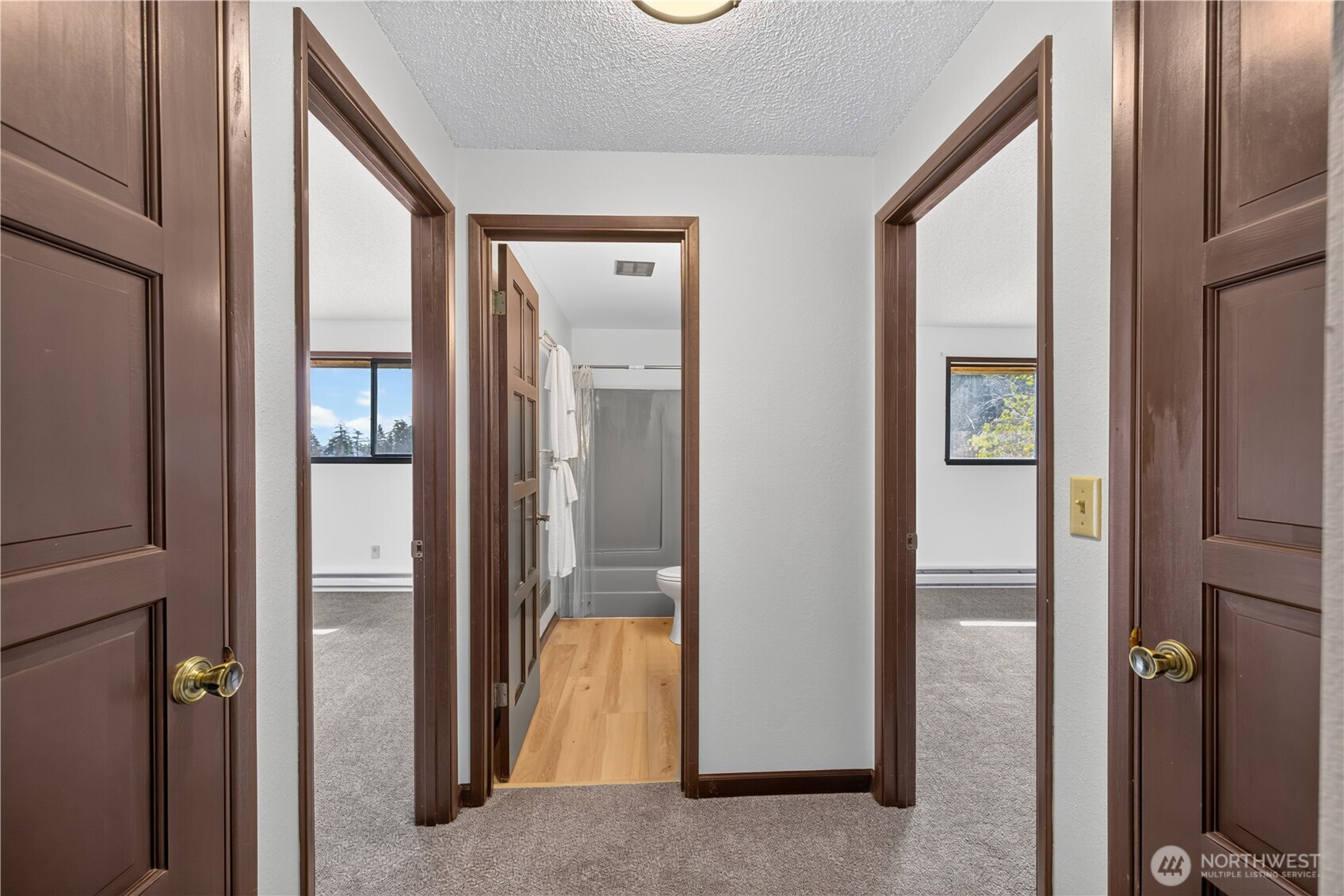 Hallway with dark wood trim and open doorways to a bathroom and two carpeted rooms.