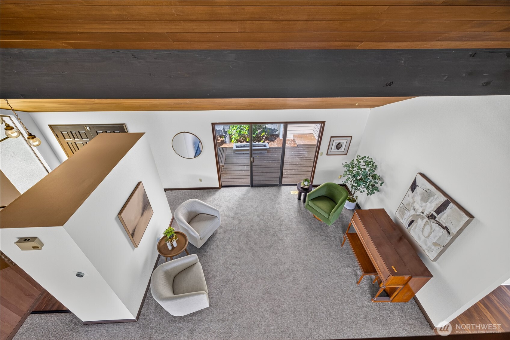 Furnished living room with exposed wood beams, gray carpet, and sliding doors to a deck.