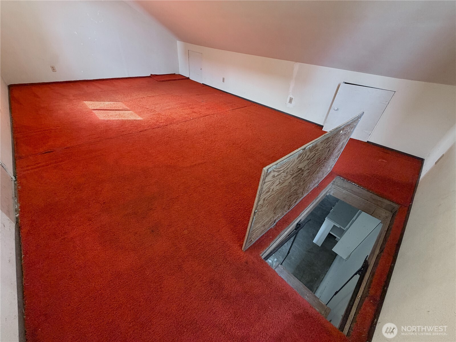 Empty carpeted upper-level room with sloped ceilings and an open floor hatch.