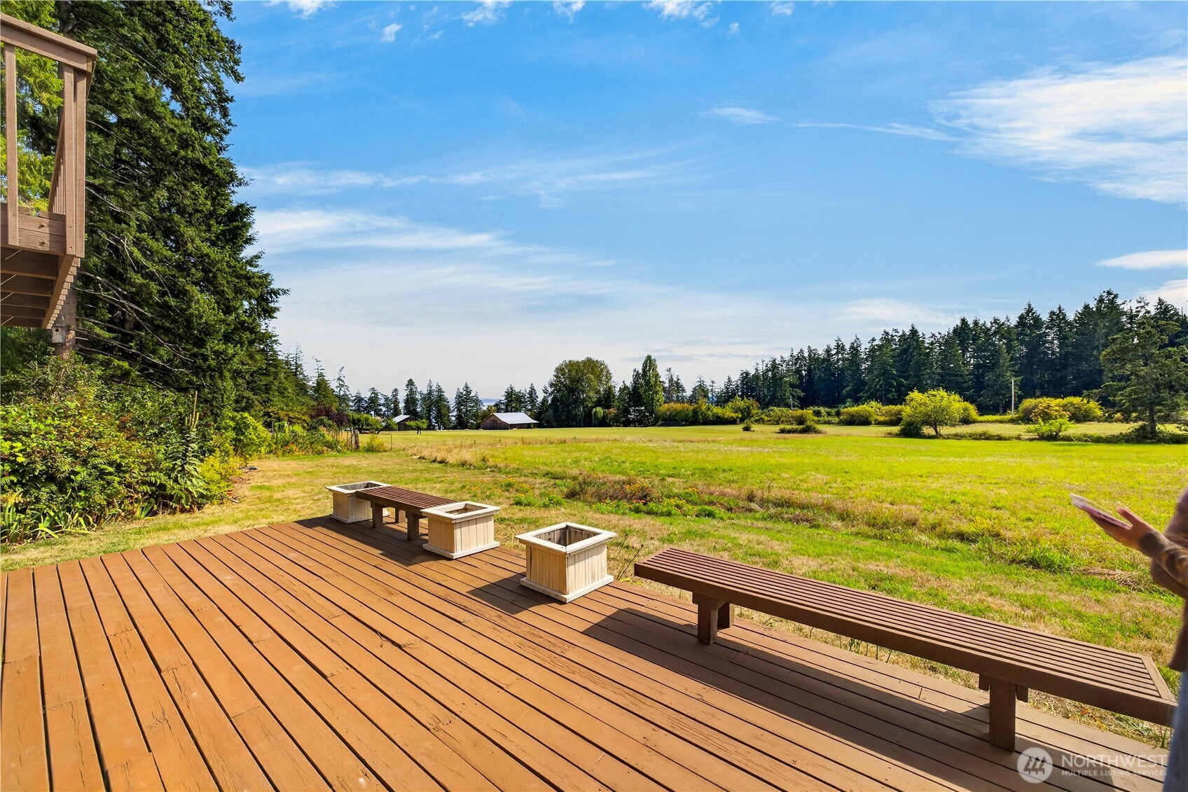 Wooden deck with benches and planters overlooking an open grassy field and tree line.