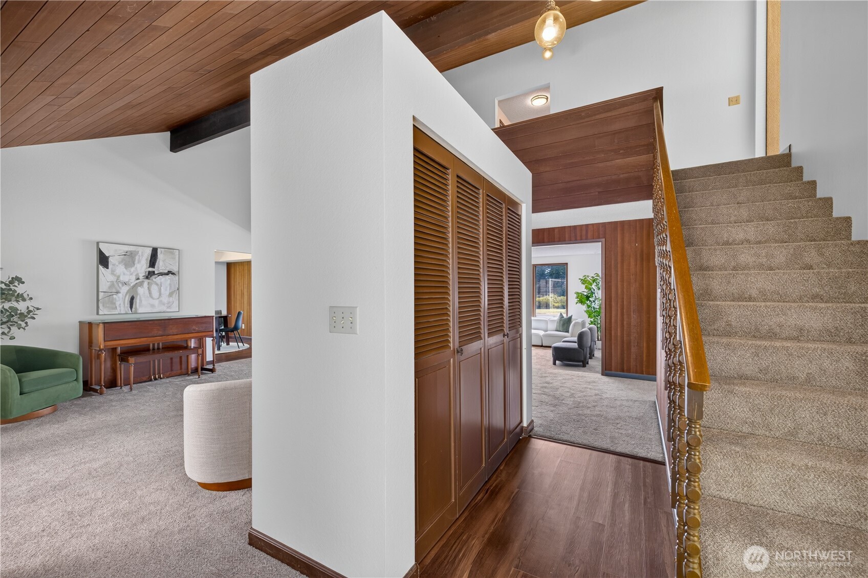 Furnished interior with a carpeted staircase, carved wood railing, and vaulted wood ceiling.