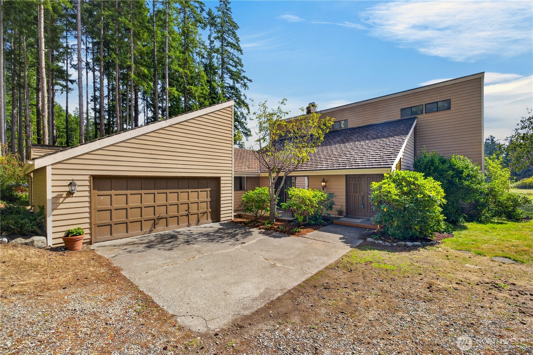 Tan contemporary home with angular rooflines, a two-car garage, and tall evergreen trees.