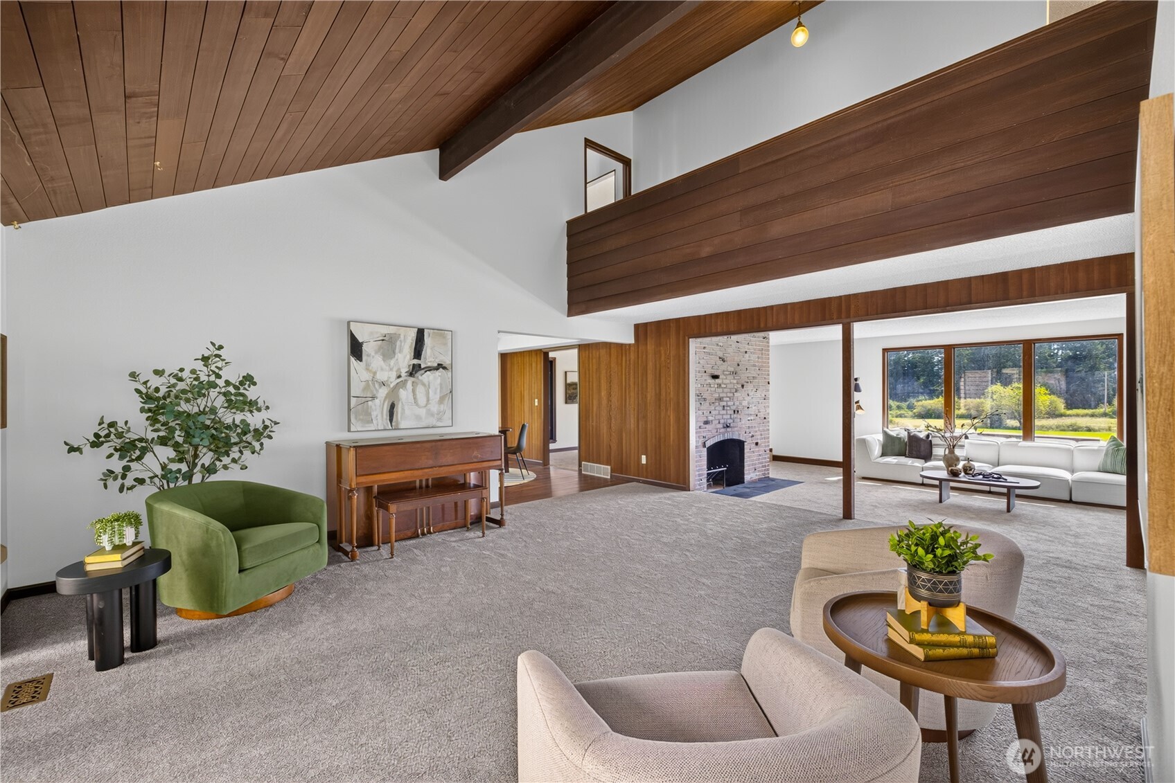 Furnished living room with a vaulted wood ceiling, brick fireplace, and large garden-facing windows.
