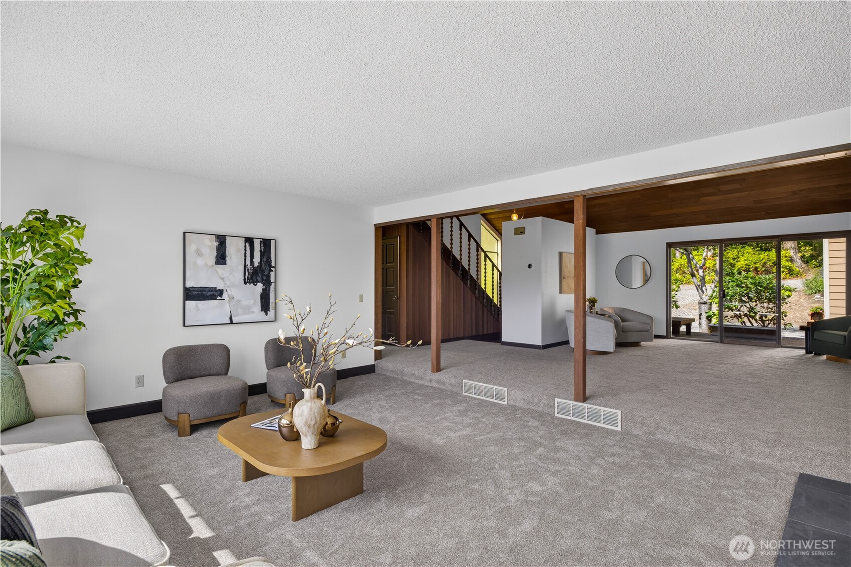 Living room with gray carpet, exposed wood beams, a staircase, and sliding glass doors to a garden.