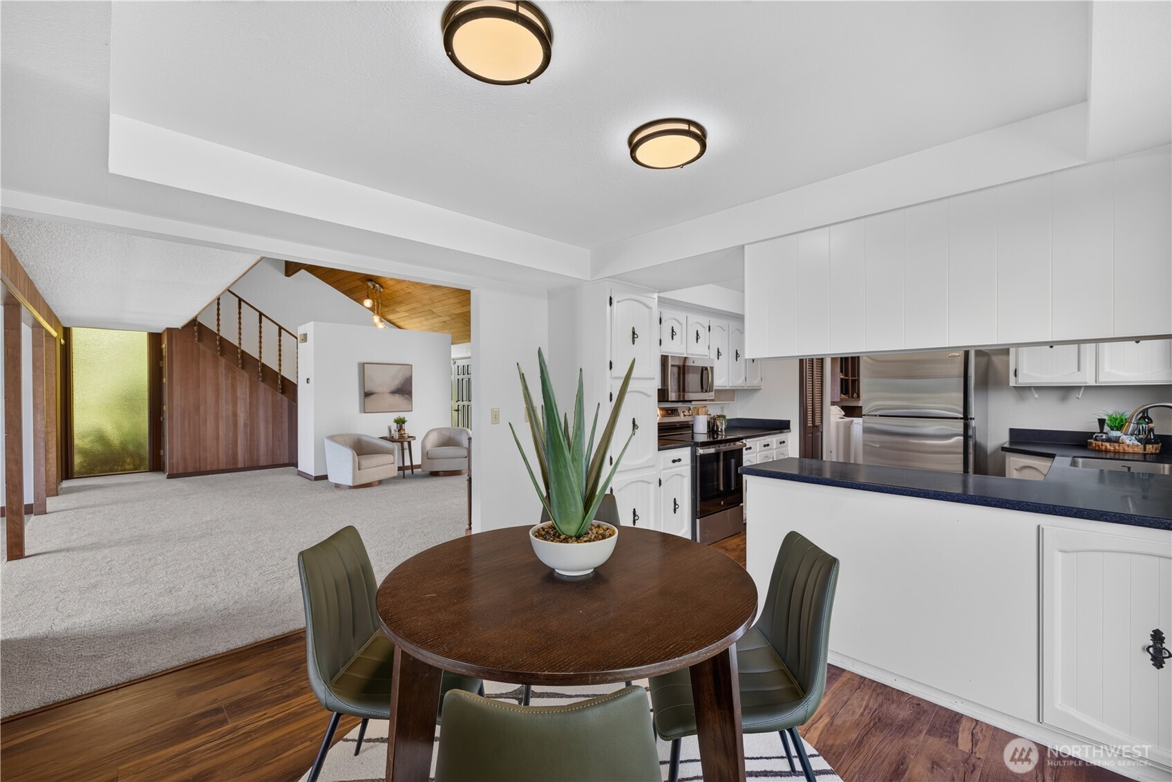 Open-plan kitchen and dining area with white cabinets, stainless appliances, and a round table with green chairs.