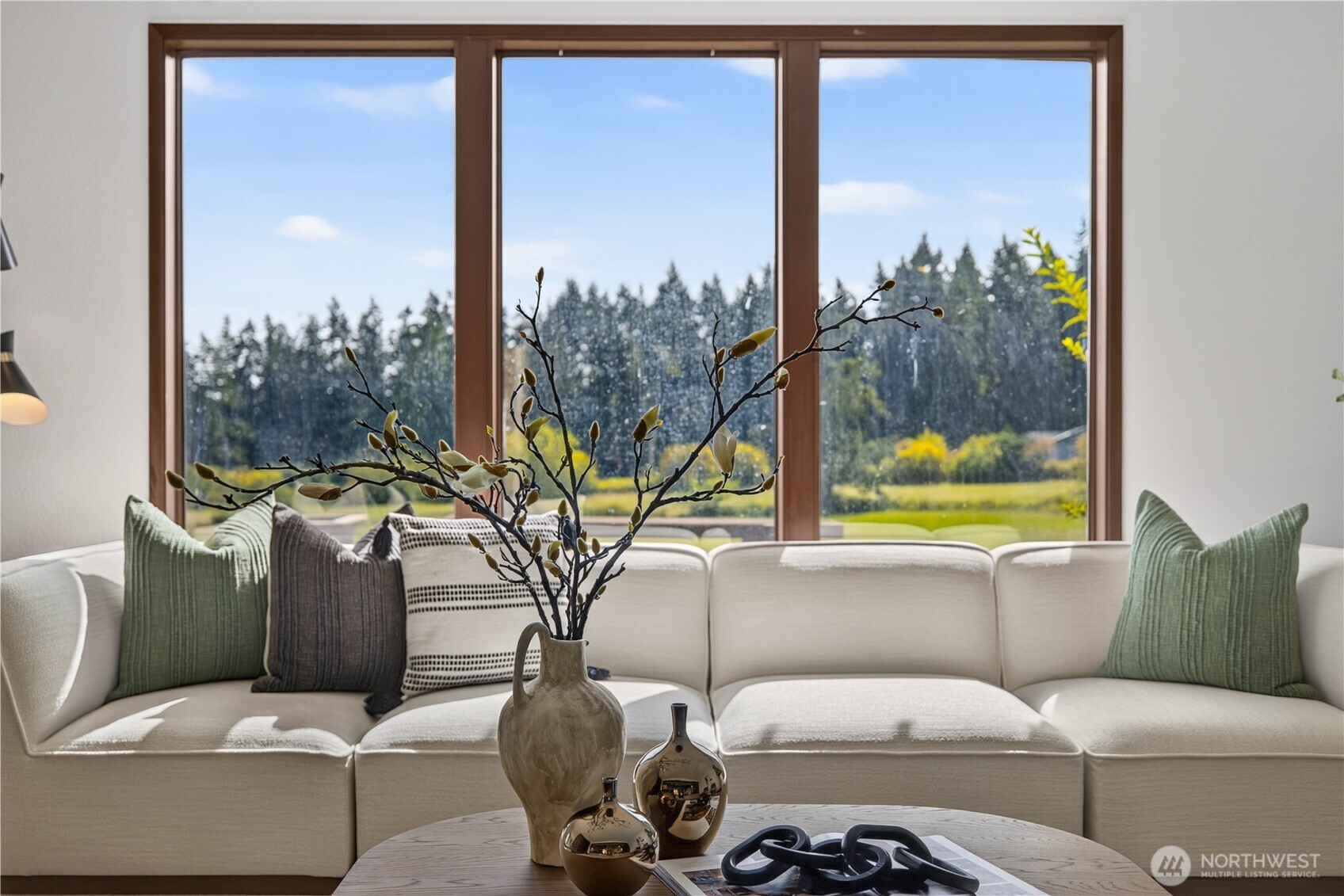 Staged living room with a cream sectional and large windows overlooking a green lawn and trees.