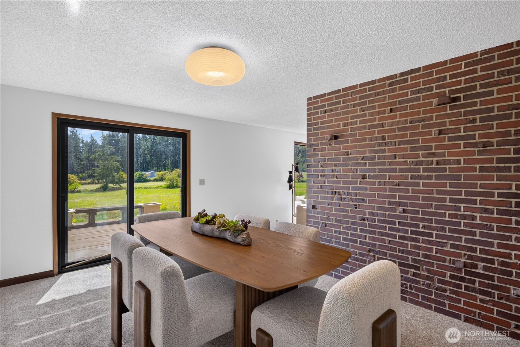 Dining room with a wood table, upholstered chairs, exposed brick wall, and sliding doors to a deck.