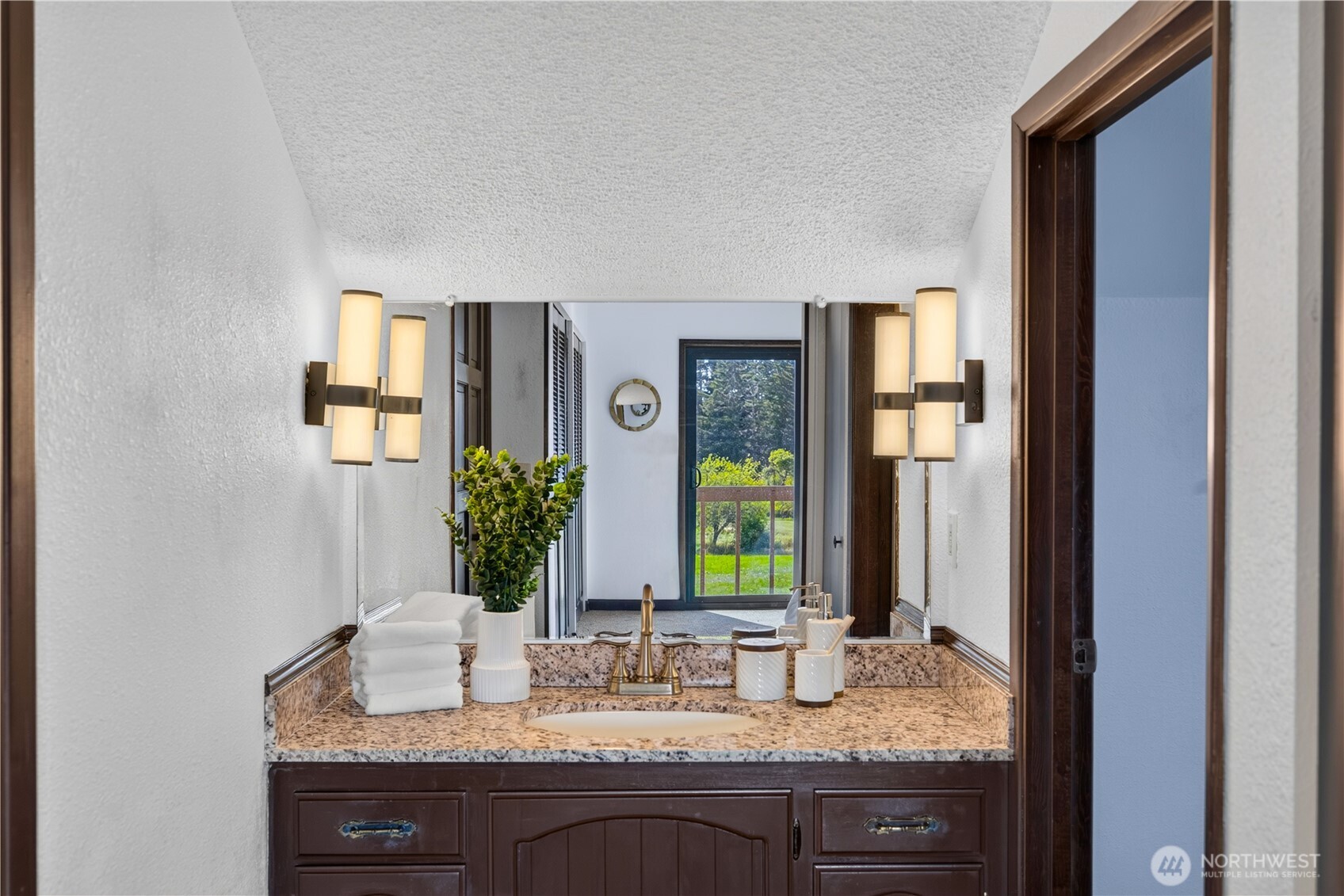 Bathroom vanity with a speckled stone counter, dark wood cabinetry, and illuminated wall sconces.