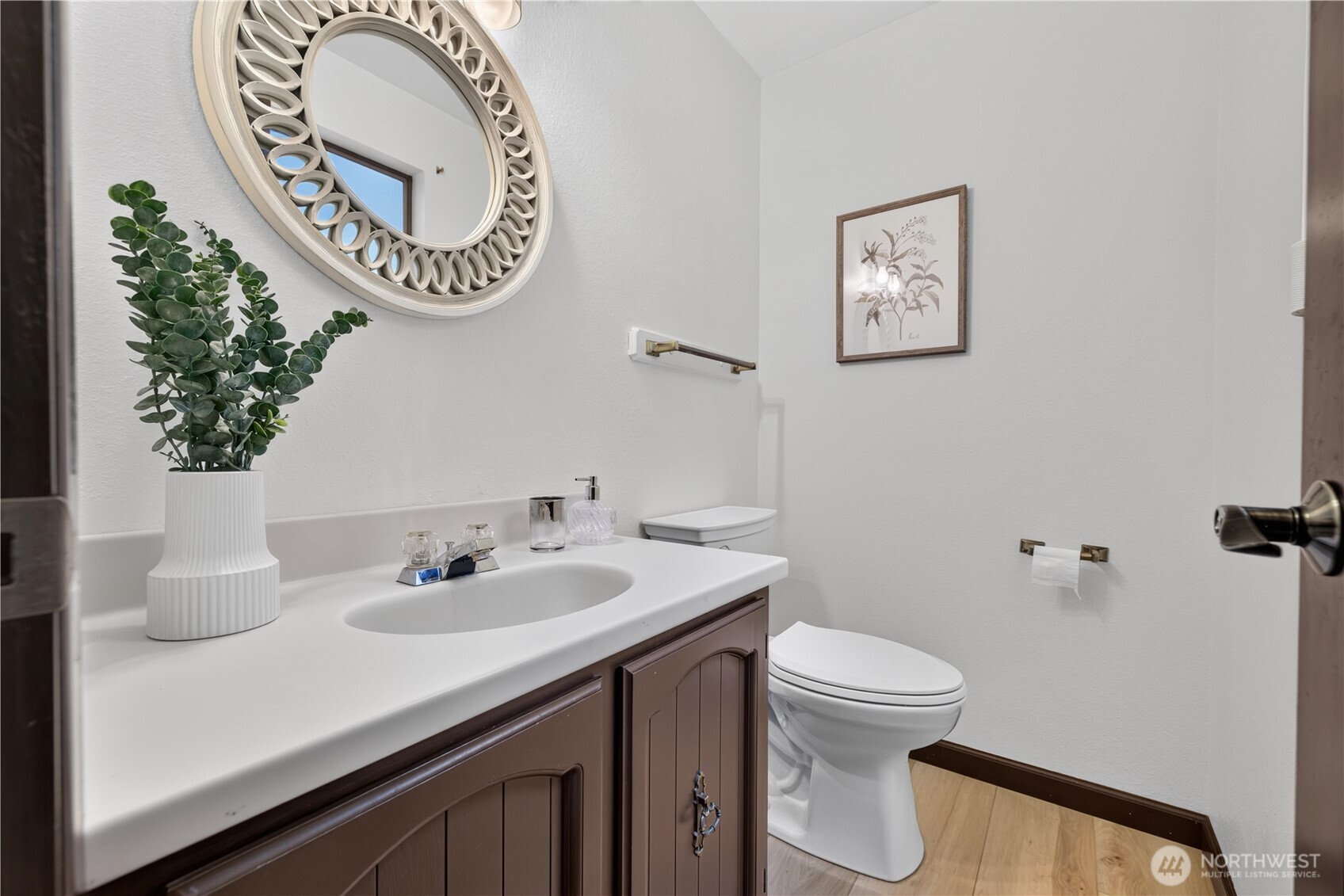 Bathroom with a dark wood vanity, white sink, toilet, and large round decorative mirror.