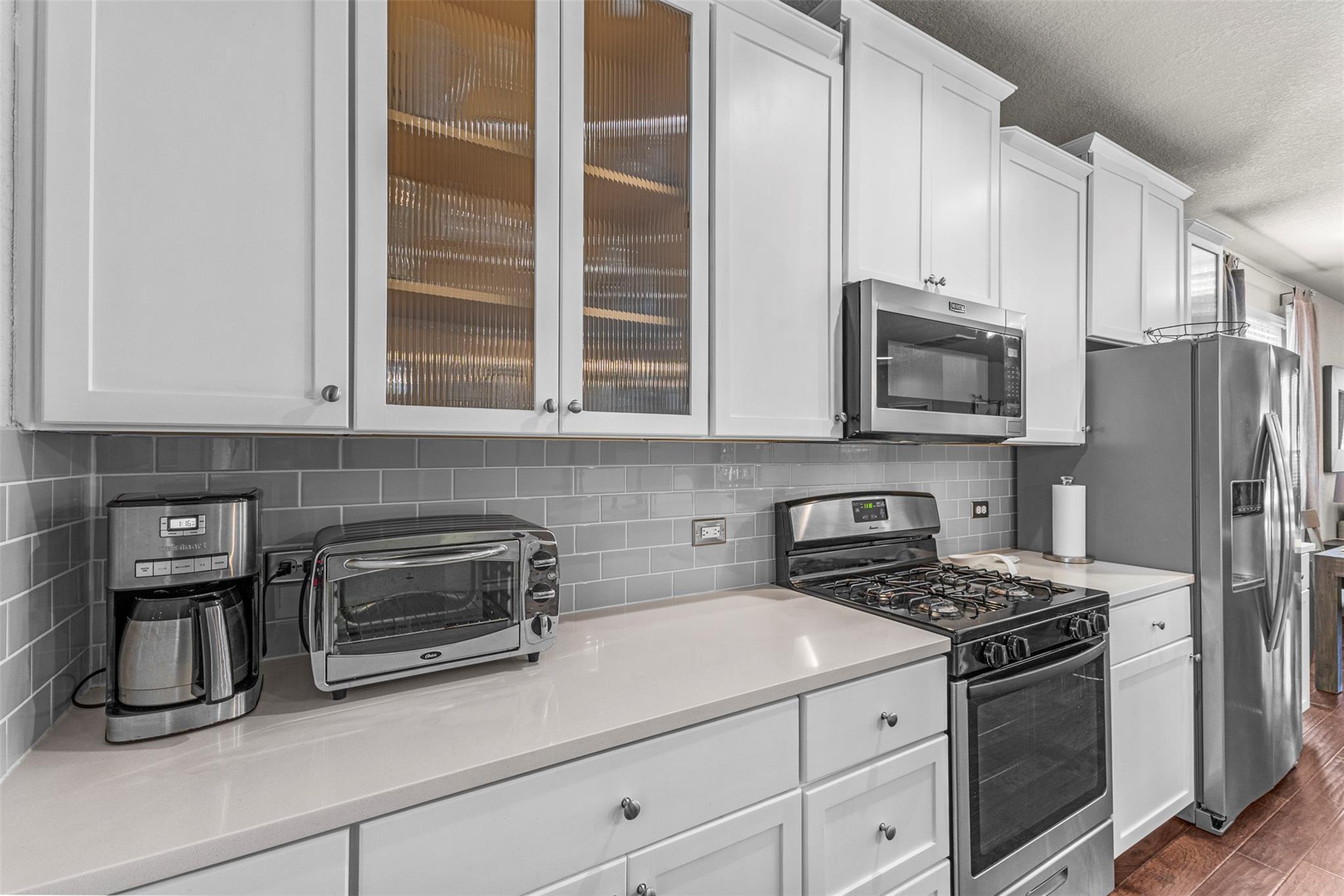 Kitchen with white cabinets, gray tile backsplash, stainless appliances, and a gas range.