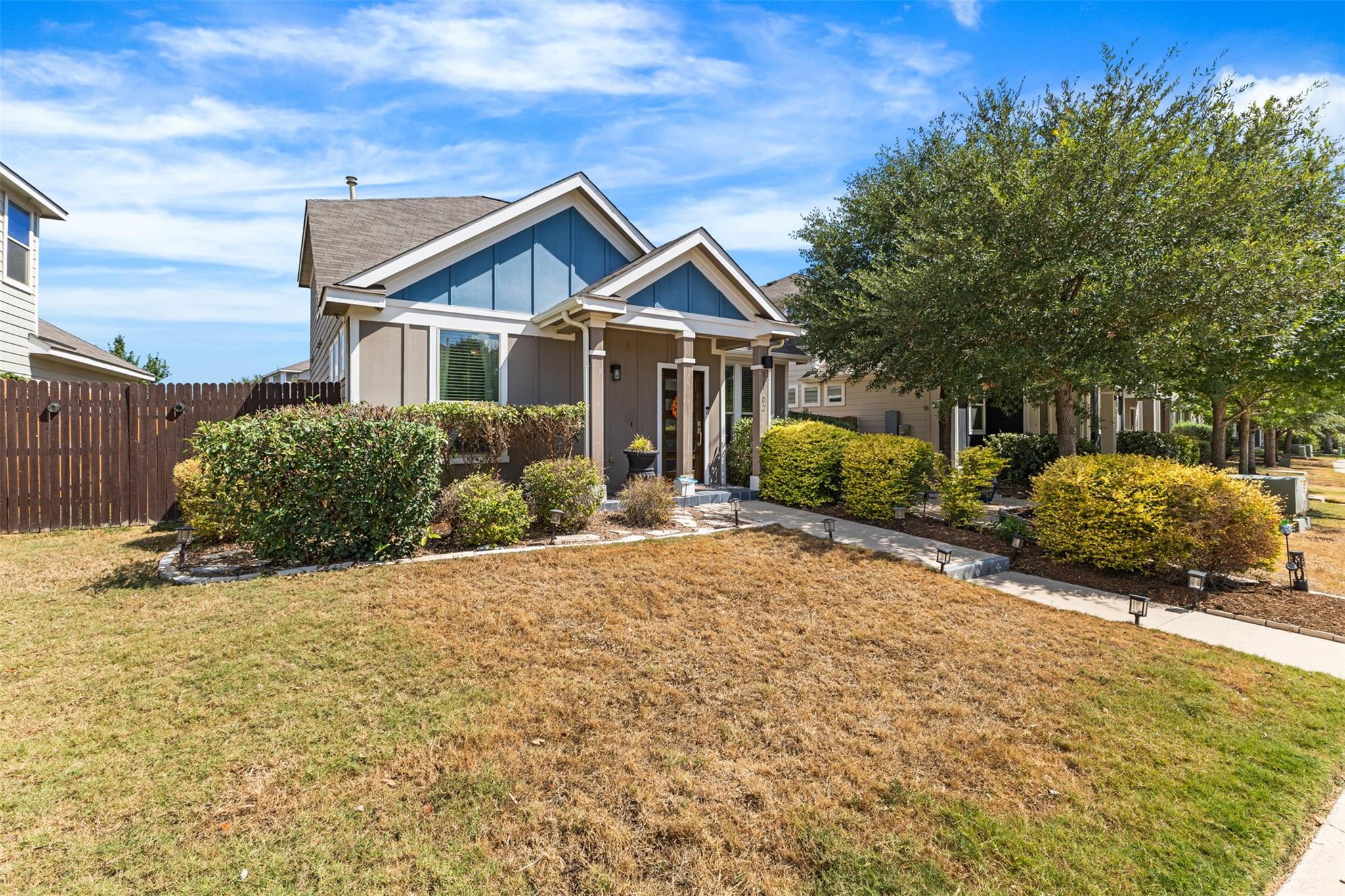 Home exterior with peaked gables, landscaped shrubs, a walkway, and a broad dry lawn.