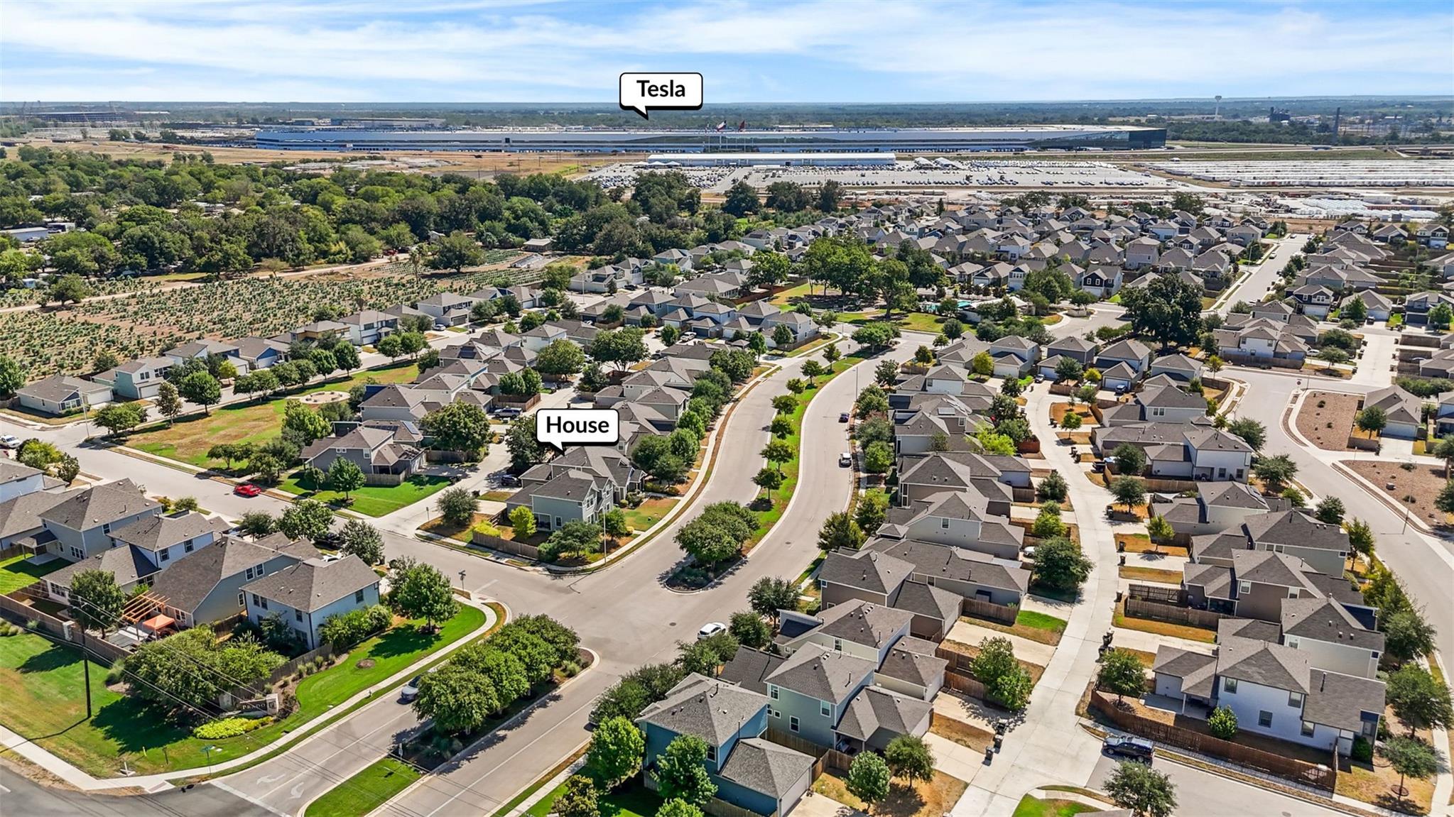 Aerial view of homes and curving streets, with the Tesla facility visible in the distance.