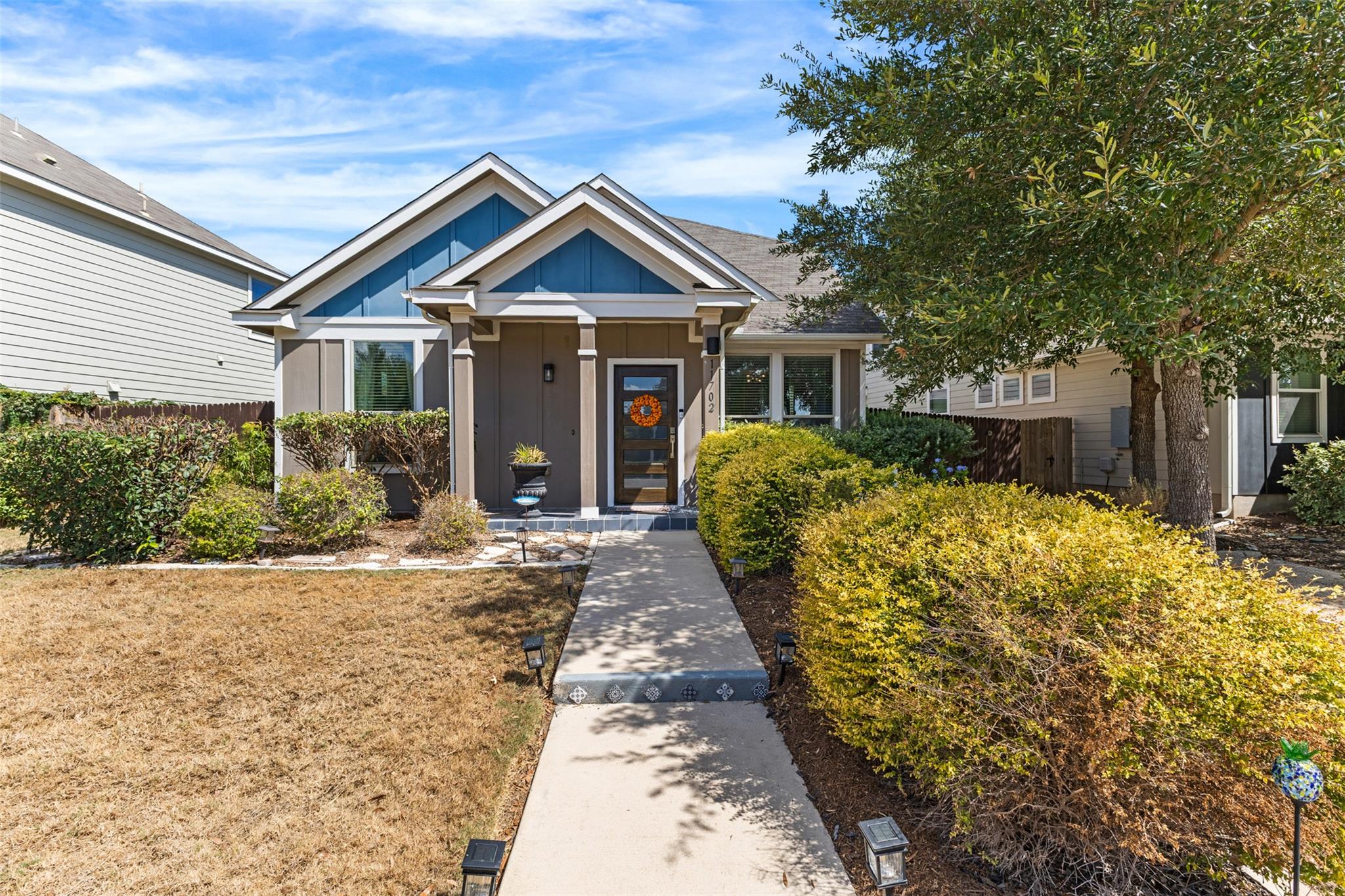 Single-story home with blue gable accents, a wreath on the front door, and a shrub-lined walkway.