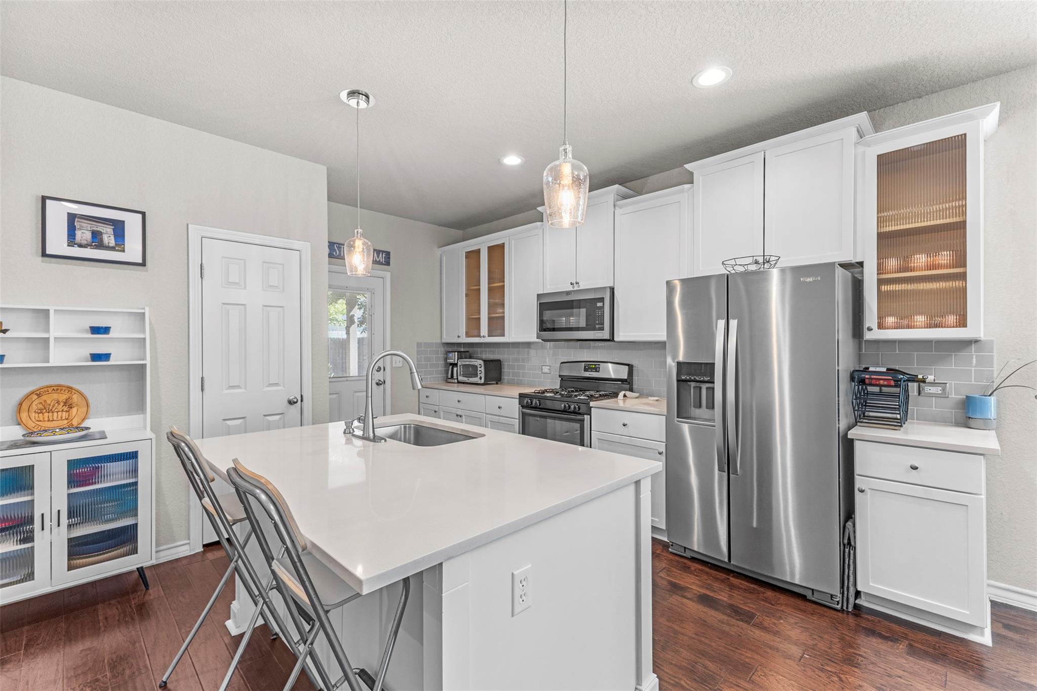 Bright kitchen with a large white island, stainless steel appliances, and dark wood flooring.