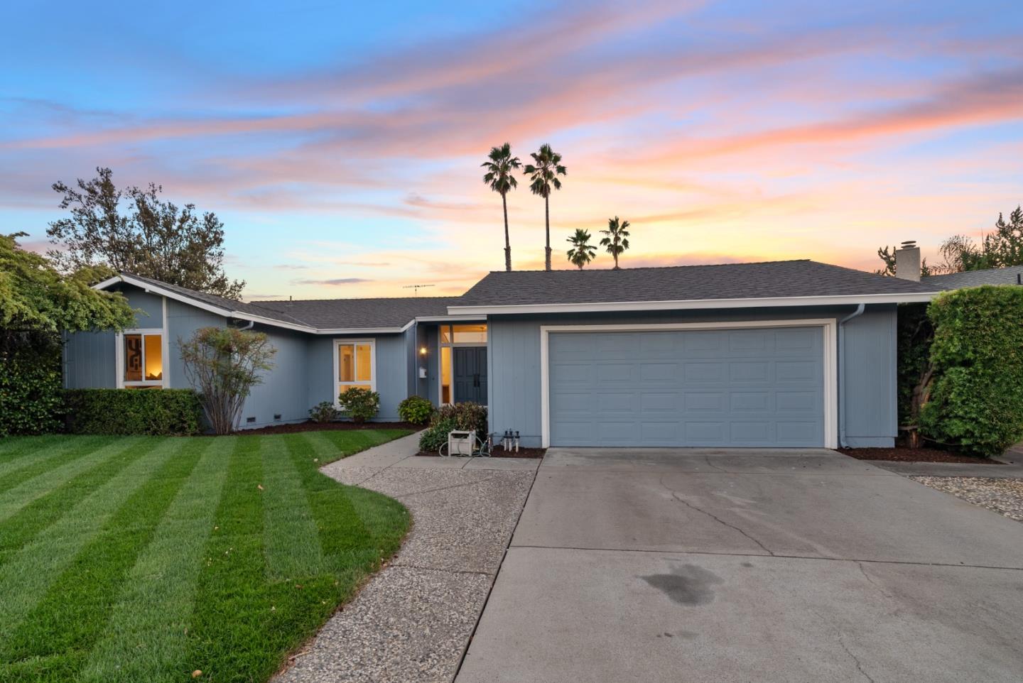 Blue-gray ranch-style home with a wide garage and manicured lawn at sunset.