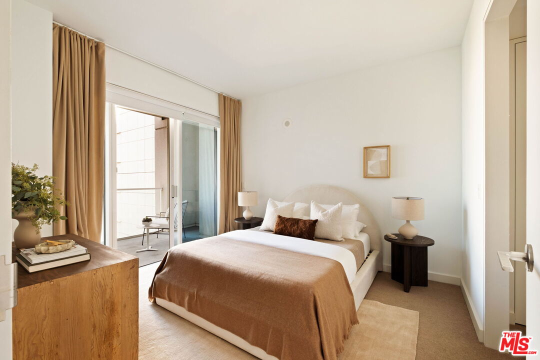 Furnished bedroom with a tan-covered bed beside sliding glass doors to a balcony.