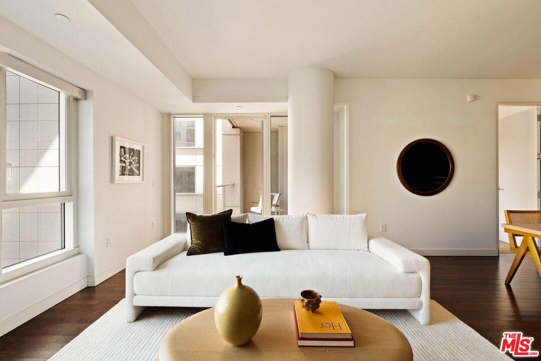 Living room with a white sofa, large windows, dark wood floors, and a round wall mirror.