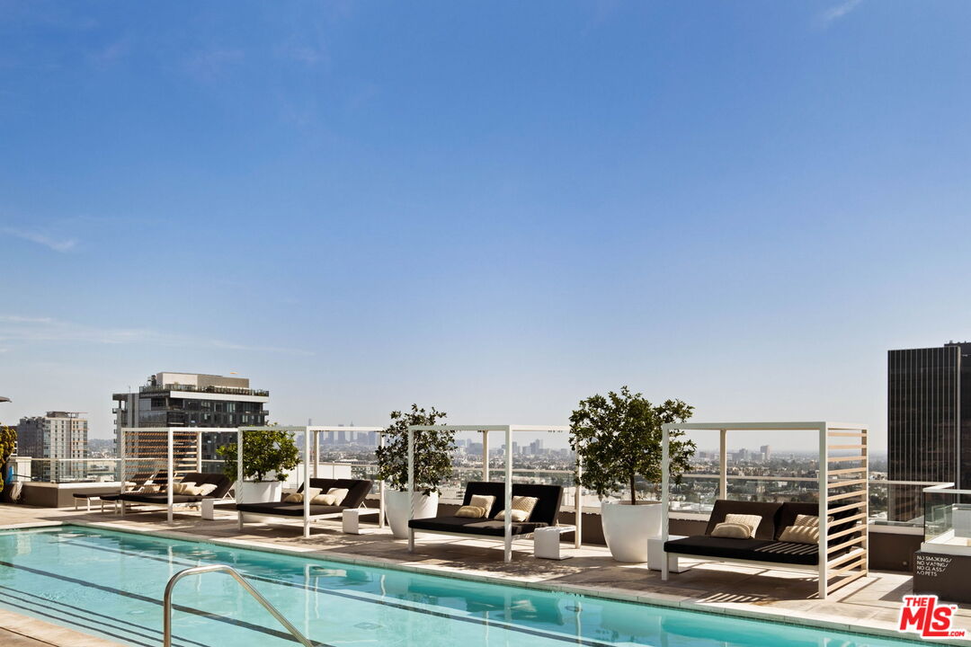 Rooftop pool beside furnished lounge seating, with potted trees and views of the Los Angeles skyline.