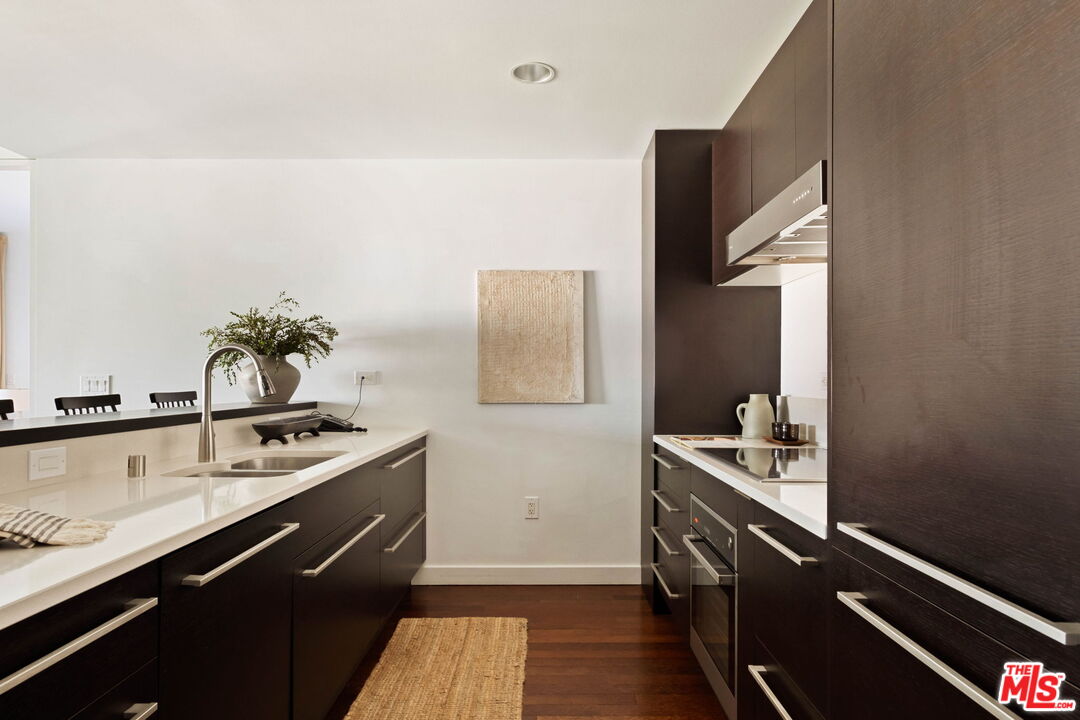 Modern kitchen with dark wood cabinetry, white counters, and stainless steel appliances.
