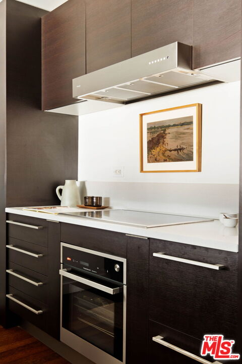 Modern kitchen with dark wood cabinets, white counters, an induction cooktop, and built-in oven.