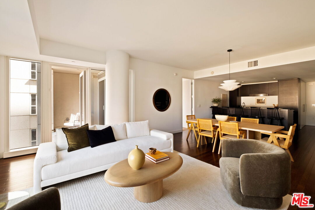 Open-plan condo living room with a white sofa, oval wood coffee table, and dining area beside the kitchen.