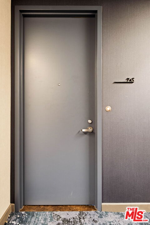 Gray entrance door with a peephole and handle, marked 7G beside the door.