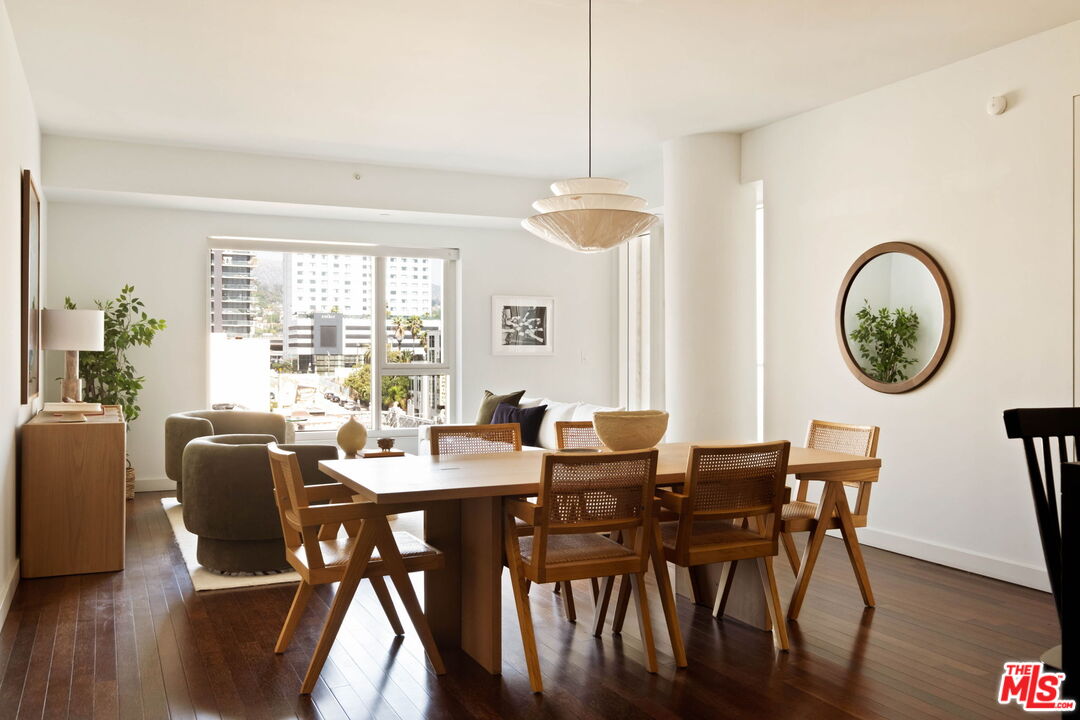 Open-plan dining and living area with a wooden dining table and large city-facing windows.