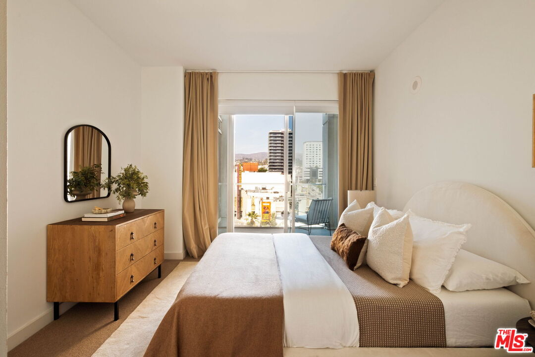 Furnished bedroom with a large bed and sliding glass doors opening to a city-view balcony.