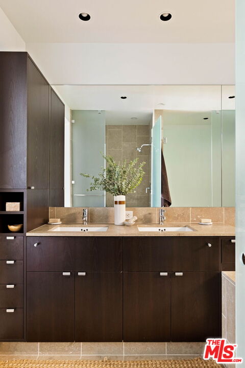 Bathroom vanity with two sinks, dark wood cabinets, a stone counter, and a wide mirror.