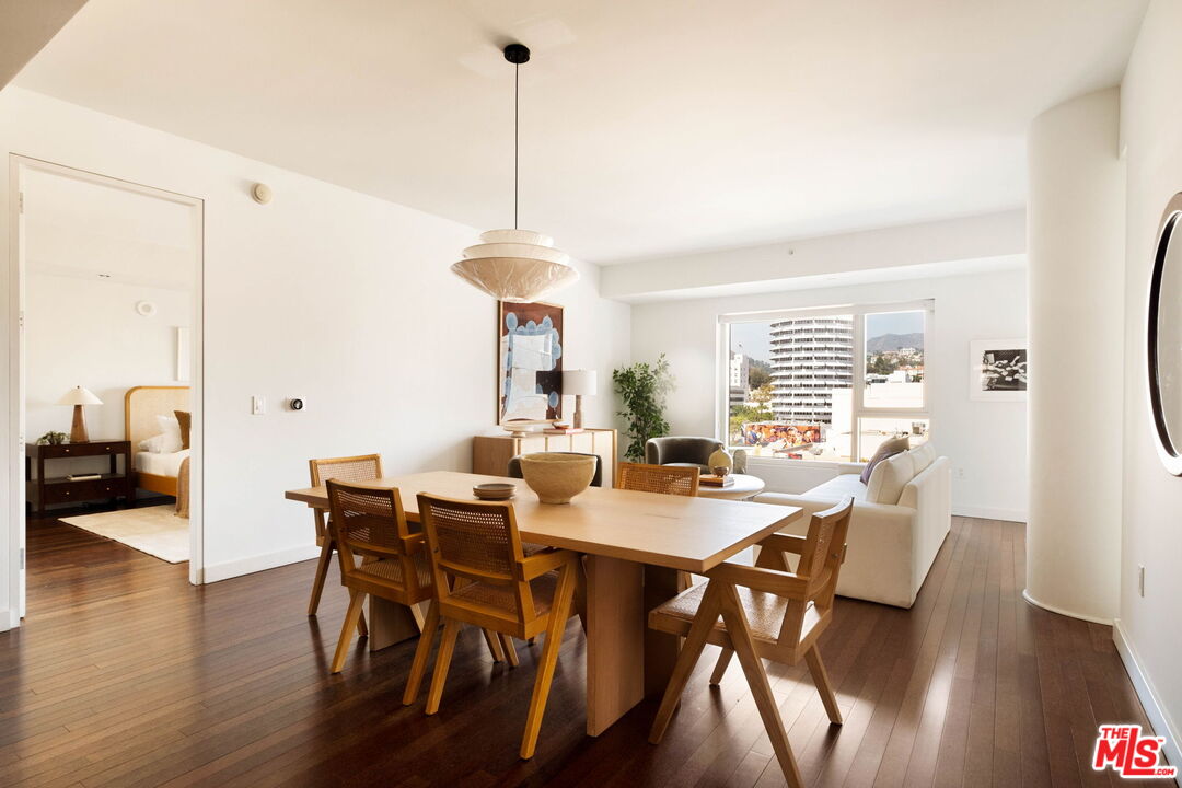 Dining area with a long wooden table and woven chairs beside a bright living room.