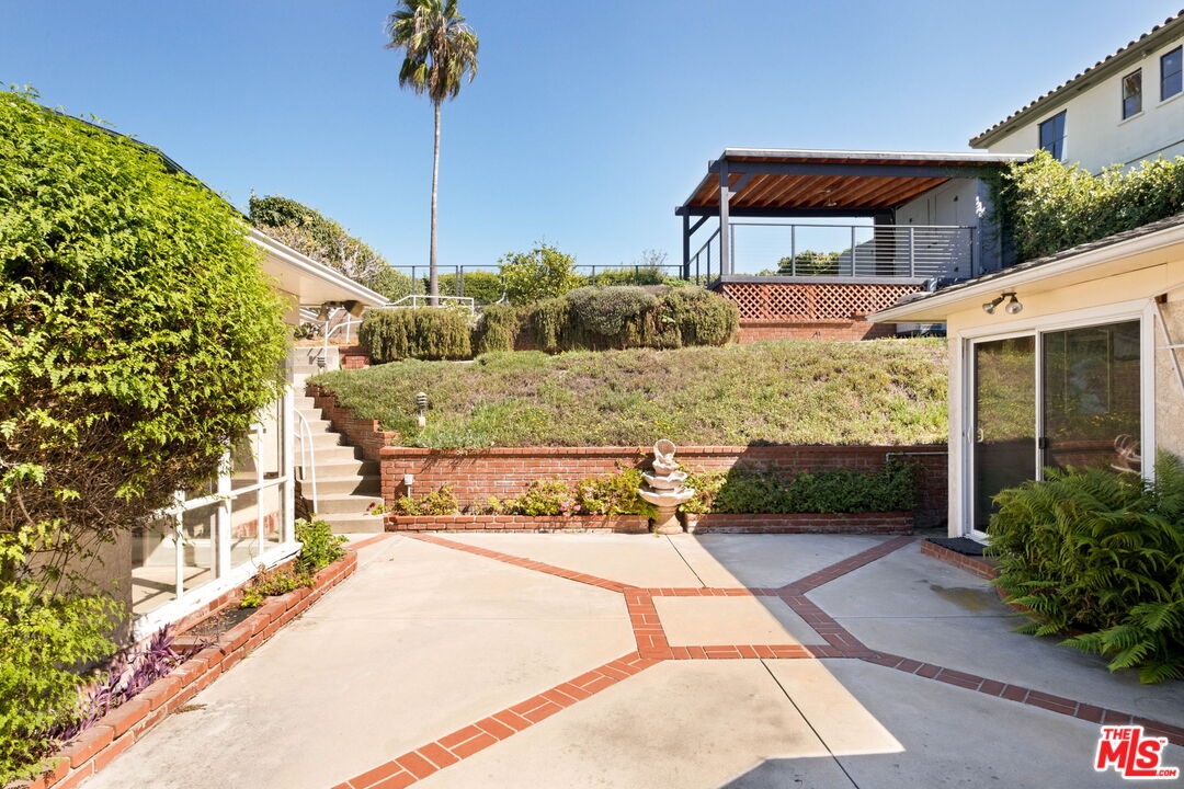 Courtyard patio with brick-edged paving, terraced garden, fountain, and covered pergola.