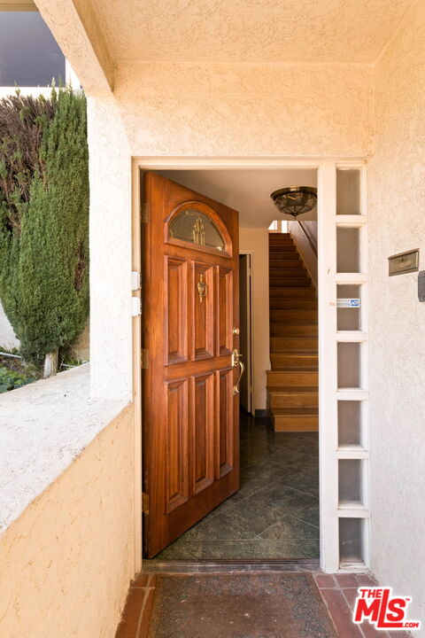 Open wooden front door reveals a staircase beyond a tiled porch.
