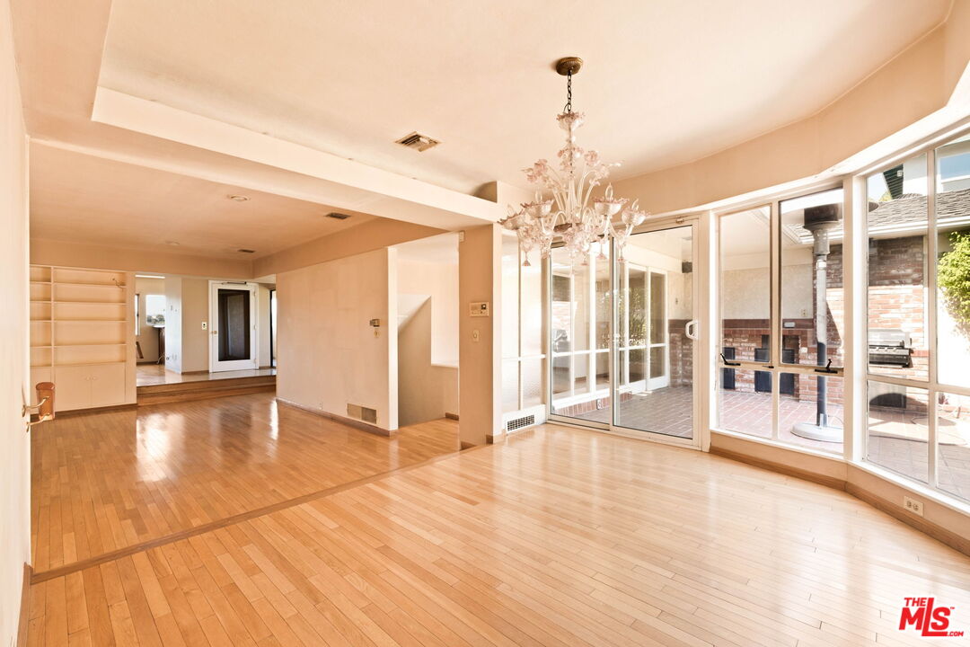Empty hardwood living and dining area with a chandelier and glass doors opening to a brick patio.