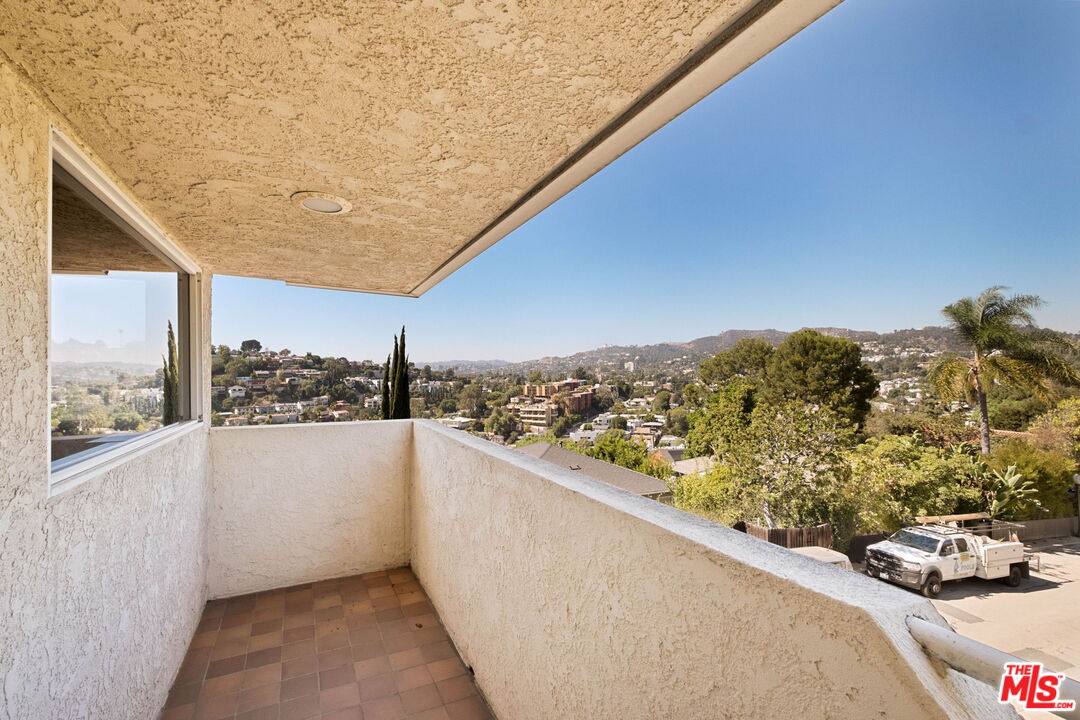 Tiled balcony overlooking a tree-filled hillside neighborhood.