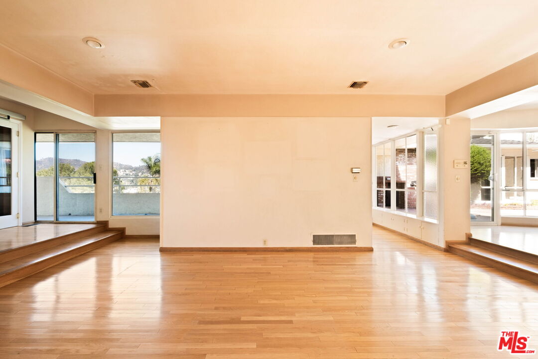 Vacant living room with hardwood floors, raised window areas, and distant hillside views.