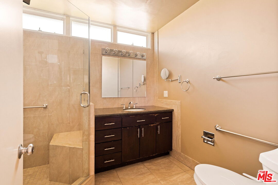 Bathroom with a glass-enclosed tiled shower, dark wood vanity, and high windows.