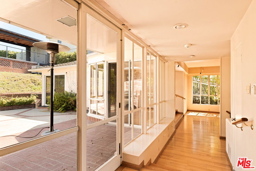 Bright hallway with hardwood floors, built-in bench, and glass doors overlooking a brick patio.