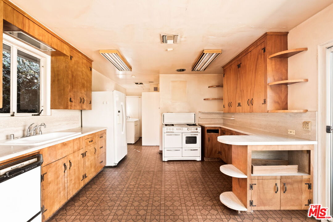 Older kitchen with wood cabinets, a central white range, patterned tile flooring, and a curved peninsula.